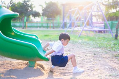 Asyalı çocuk bahçesi yaz, mutlu çocuk anaokulu veya okul öncesi okul bahçesinde ışığında altında slayt oynayan.