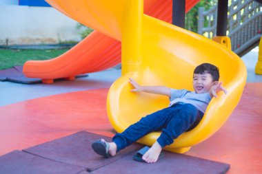 Asyalı çocuk bahçesi içinde güneş ışığı altında slayt oynayan 