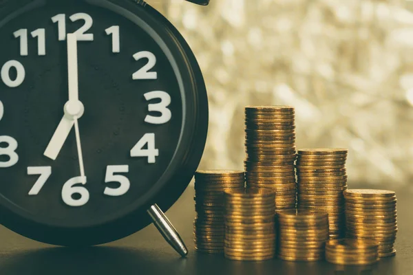 Relógio de alarme e pilhas de moedas na mesa de trabalho, tempo de poupança — Fotografia de Stock