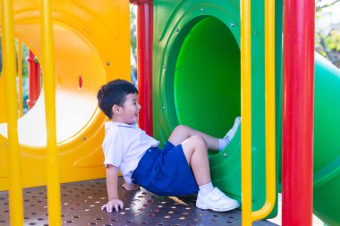 Asyalı çocuk bahçesi içinde güneş ışığı altında slayt oynayan 