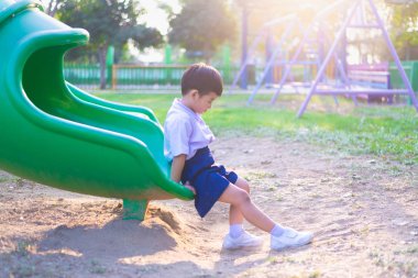 Asyalı çocuk bahçesi içinde güneş ışığı altında slayt oynayan 