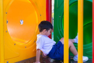 Asyalı çocuk bahçesi içinde güneş ışığı altında slayt oynayan 