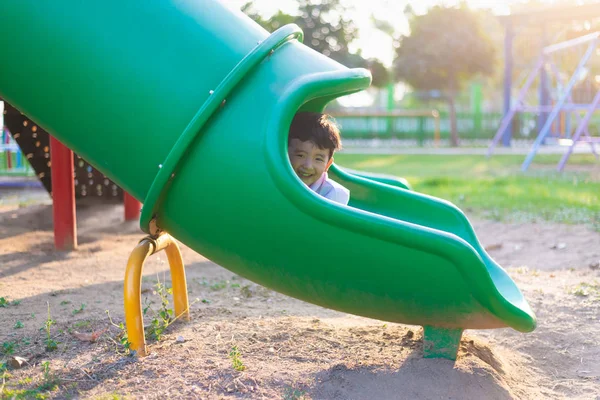 Asiático niño jugando diapositiva en el parque infantil bajo la luz del sol en — Foto de Stock
