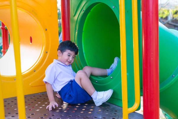 Asiático niño jugando diapositiva en el parque infantil bajo la luz del sol en — Foto de Stock