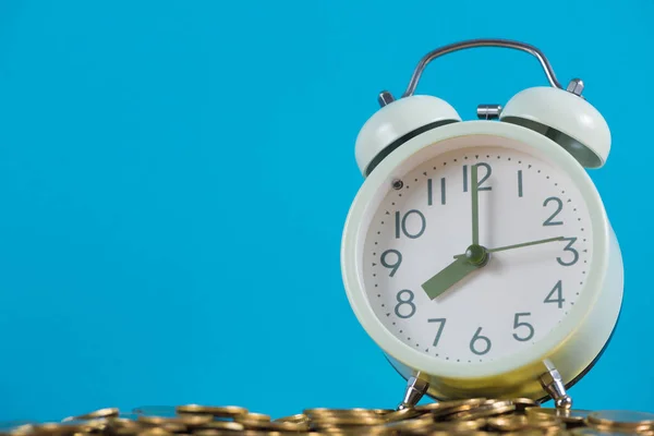 Reloj despertador vintage en la pila de moneda de oro con fondo azul —  Fotos de Stock