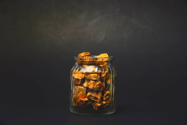 Nuggets de oro o mineral de oro y frasco de vidrio en habitación oscura . — Foto de Stock