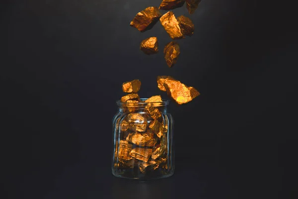Caída de pepitas de oro o mineral de oro y frasco de vidrio en habitación oscura — Foto de Stock