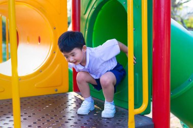 Asyalı çocuk bahçesi içinde güneş ışığı altında slayt oynayan 