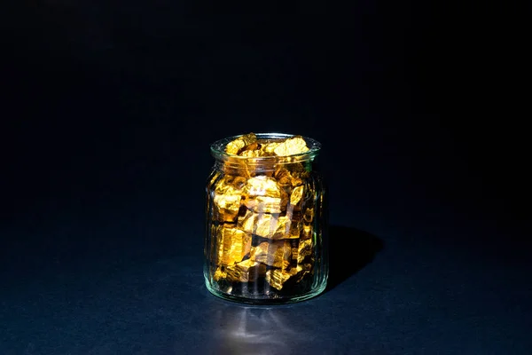 Gold nuggets or gold ore and glass jar in dark room.
