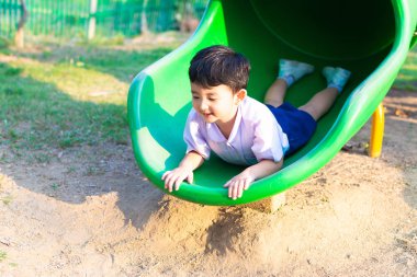 Asyalı çocuk bahçesi içinde güneş ışığı altında slayt oynayan 