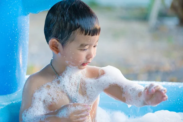 暑い夏の日にインフレータブルベビープールで水と泡で遊ぶアジアの少年 焦点が浅い — ストック写真