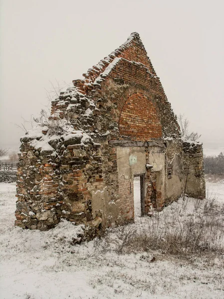 Remains of an old peaked, triangular shape building made of bricks in the falling snow.