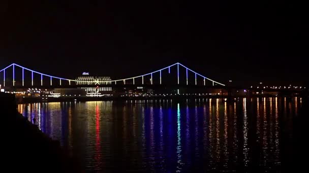 夜照在桥上 美丽的桥在夜色中照亮了城市的夜景 夜时的天桥 基辅的行人桥在河边的 Dnepr 在夜色中倒映在水中 — 图库视频影像