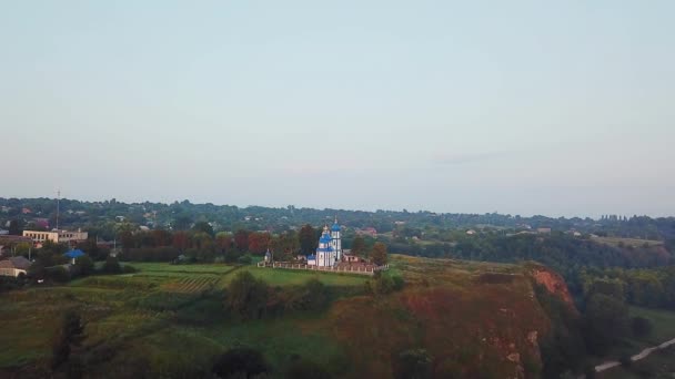 日の出の丘の上の教会の航空写真 橋と教会を背景に夜明けの川の空中ビュー 日の出時の朝霧 — ストック動画