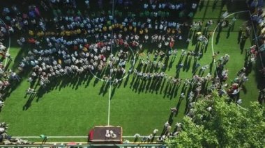 Okul stadyumunda dans eden çocukların hava görüntüsü, şehirdeki okul stadyumundaki çocukların hava görüntüsü, oyuncu çocukların üzerinden uçan insansız hava aracı, açık hava futbol sahası görüntüleri.