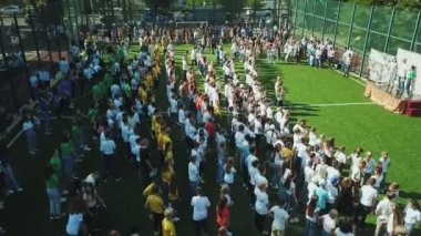Okul stadyumunda dans eden çocukların hava görüntüsü, şehirdeki okul stadyumundaki çocukların hava görüntüsü, oyuncu çocukların üzerinden uçan insansız hava aracı, açık hava futbol sahası görüntüleri.