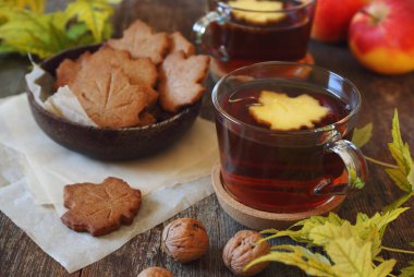 Sonbahar ruh hali: tarçınlı kurabiye şeklinde akçaağaç yaprakları, fincan çay, kırmızı elma ve sarı yapraklar. Tonlu görüntü
