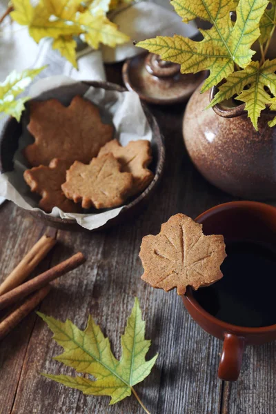 Autumn mood. Cinnamon cookies in form of maple leaves, cup of coffee and yellow leaves. Toned image