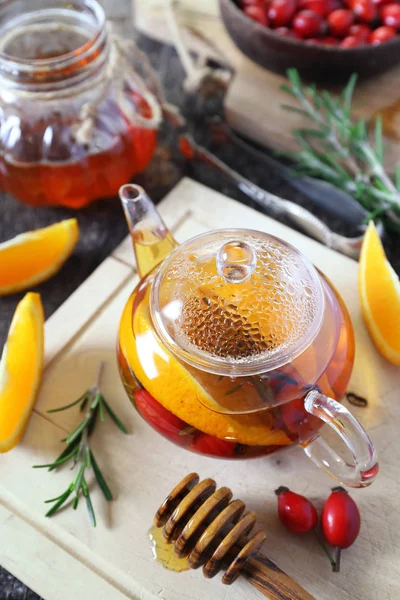 Healthy hot winter beverage. Rose hip tea with oranges in teapot, rosemary and berries