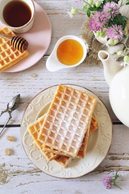 Belçika waffle 'ı ve bal, yonca çiçekli tatlı bahar kahvaltısı için bir fincan çay. Üst görünüm