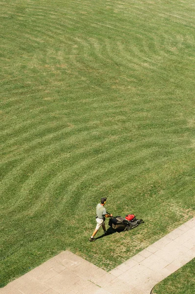 Man works with lawn mower on the wide field. Top view background. Space for text for web sites, brochures, advertising. Sunny weather and bright warm colors. Grass line pattern. Finished work outside