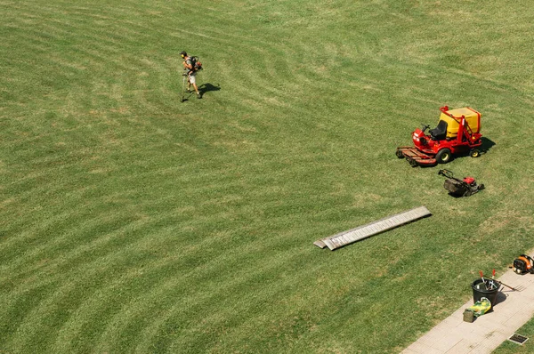 Man works with lawn mower on the wide field. Top view background. Space for text for web sites, brochures, advertising. Sunny weather and bright warm colors. Grass line pattern. Finished work outside