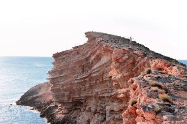 Adam uçurumun kenarında ayakta, epik yatay. Gün batımı gündüz su yansıması ile. Deniz ve kırmızı, sonsuz görünümü dağlar taşlar. Yaz spor tecrübe hiking. Doğal güzelliği ile gerçek dışı konumu.