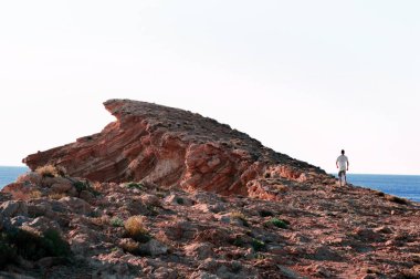 Adam uçurumun kenarında ayakta, epik yatay. Gün batımı gündüz su yansıması ile. Deniz ve kırmızı, sonsuz görünümü dağlar taşlar. Yaz spor tecrübe hiking. Doğal güzelliği ile gerçek dışı konumu.