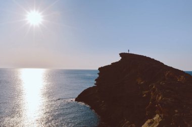 Adam uçurumun kenarında ayakta, epik yatay. Gün batımı gündüz su yansıması ile. Deniz ve kırmızı, sonsuz görünümü dağlar taşlar. Yaz spor tecrübe hiking. Doğal güzelliği ile gerçek dışı konumu.