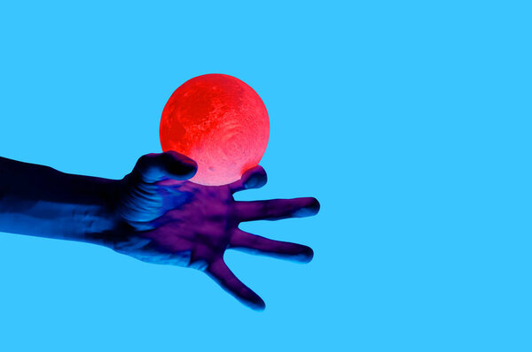 Isolated on blue background photo of man holding moon shape illuminated sphere. 