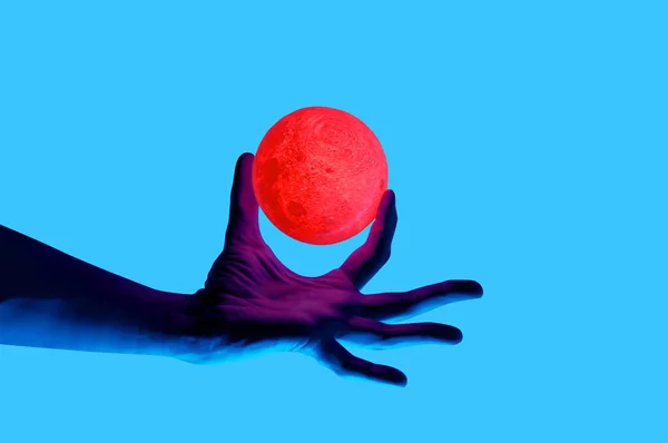 Isolated on blue background photo of man holding moon shape illuminated sphere.