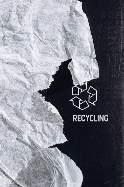 Baskılı beyaz geri dönüşüm logosu işareti ve geri dönüştürülmüş buruşuk kağıt parçası ile siyah dokulu karton dikey arka plan. Metin için boşluk. Minimalist stil şablonu. Kalın metin Geri Dönüşüm
