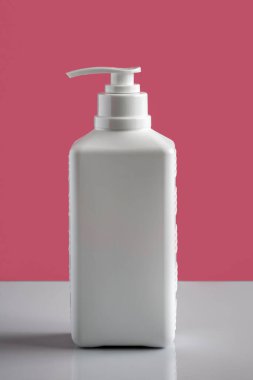 Deterjanlı beyaz plastik şişe ve pembe arka planda yansıması olan temizlik malzemeleri..