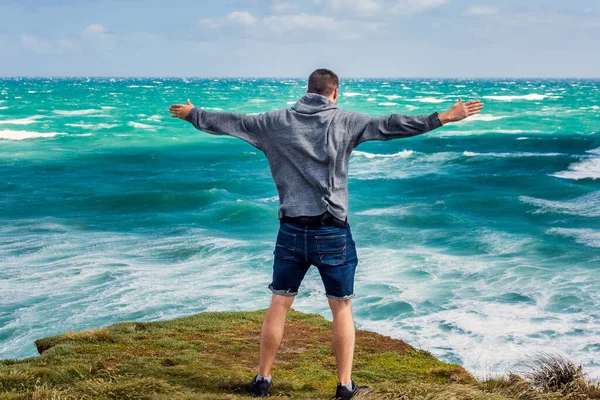 ニュージーランドのブラフの近くで巨大な波でニュージーランドの海岸で風と戦う男 — ストック写真