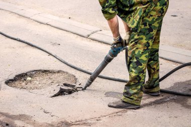 Üniformalı profesyonel işçilerin asfalt yolu matkapla tamir ederken çekilmiş bir fotoğrafı. Konsept yenileme, şehrin ana caddesinin büyük onarımı, yol inşaatı..