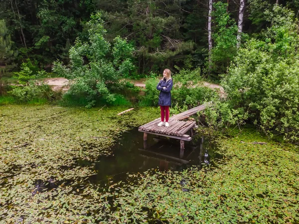 美しい少女はベラルーシのミンスク近くの自然保護区の森林湖の桟橋に座っています — ストック写真