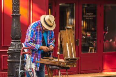 Montmartre Tepesi 'nde arkasında kırmızı duvar olan bir ressam. Geleneksel Fransız kafeleri ve sanat galerilerine sahip Montmartre, Paris 'te en çok ziyaret edilen yerlerden biridir. Paris, Fransa - 28 Temmuz 2018.