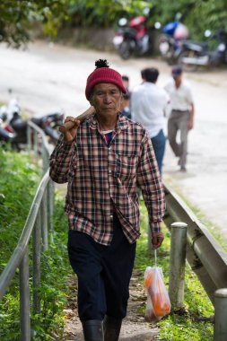 Yaşlı adam ormanda elinde bir sopayla yol kenarında yürüyor. Doi Mae Salong, Tayland - 14 Kasım 2017.