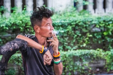 Yaşlı adam otobüs durağında sigara içiyor. Bangkok, Tayland - 09 Aralık 2017.