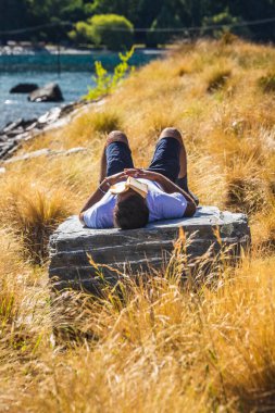 Güney Adası, Queenstown Yeni Zelanda 'da bir kayanın üzerinde yüzü kitapla uyuyan bir adam. Queenstown, Yeni Zelanda - 18 Aralık 2017.