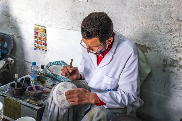 Local artisan painting on clay pot and creating handmade items in old Medina market. Fes, Morocco - April 10 2016.