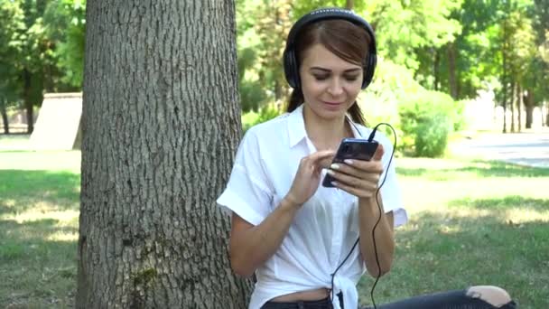 Junges Mädchen hört im Park Musik am Telefon — Stockvideo