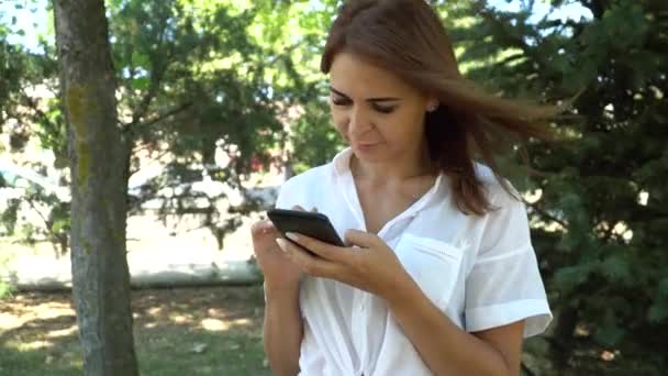 Młoda dziewczyna wpisując wiadomości tekstowych na telefon, na zewnątrz — Wideo stockowe