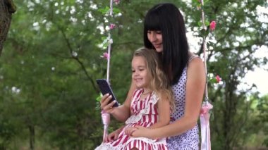 güzel genç anne ve kızı doğada telefon bakarak gülümseyerek, aile ve teknoloji kavramı