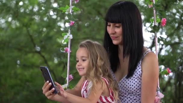 美丽的年轻母女微笑着看着手机在自然 家庭的概念和技术 — 图库视频影像