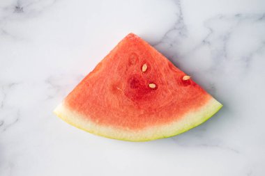 Dilimlenmiş karpuz meyvesi gri ve beyaz mermer arka planda duruyor.