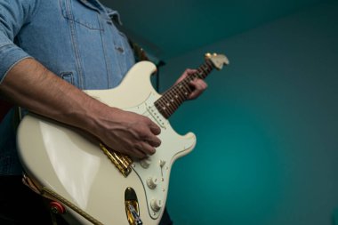 Kot ceketle beyaz elektro gitar çalan bir adam.