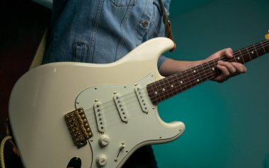 Kot ceketle beyaz elektro gitar çalan bir adam.