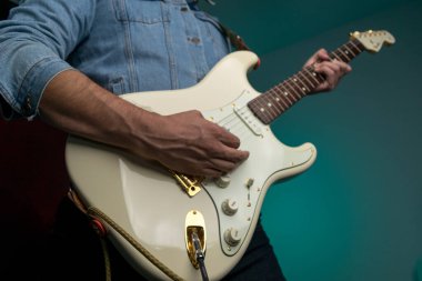 Kot ceketle beyaz elektro gitar çalan bir adam.