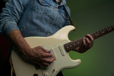 Kot ceketle beyaz elektro gitar çalan bir adam.